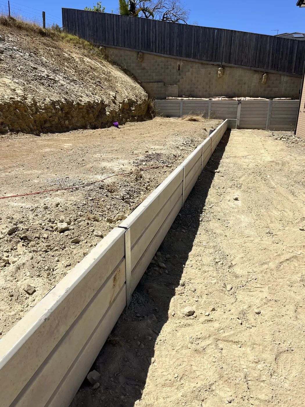 Concrete sleeper retaining wall being built along an excavated slope